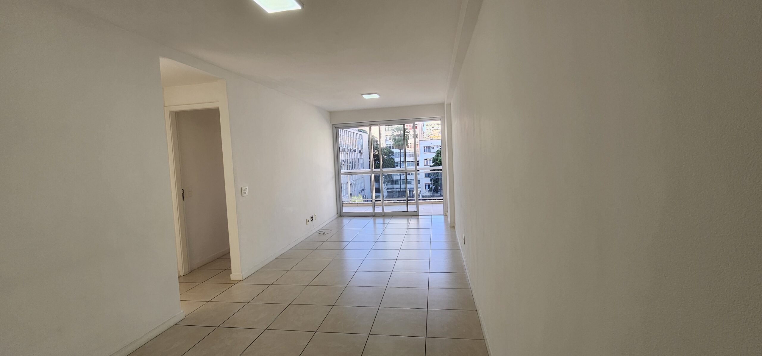 Sala com varanda ao fundo e piso de porcelanato